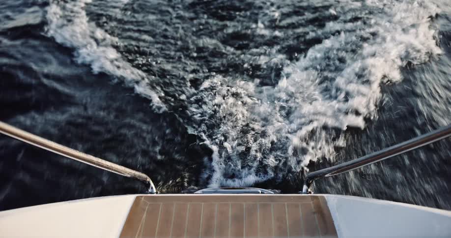 Slow-motion view from the stern of a boat as it cuts through the dark water, creating a foamy wake
