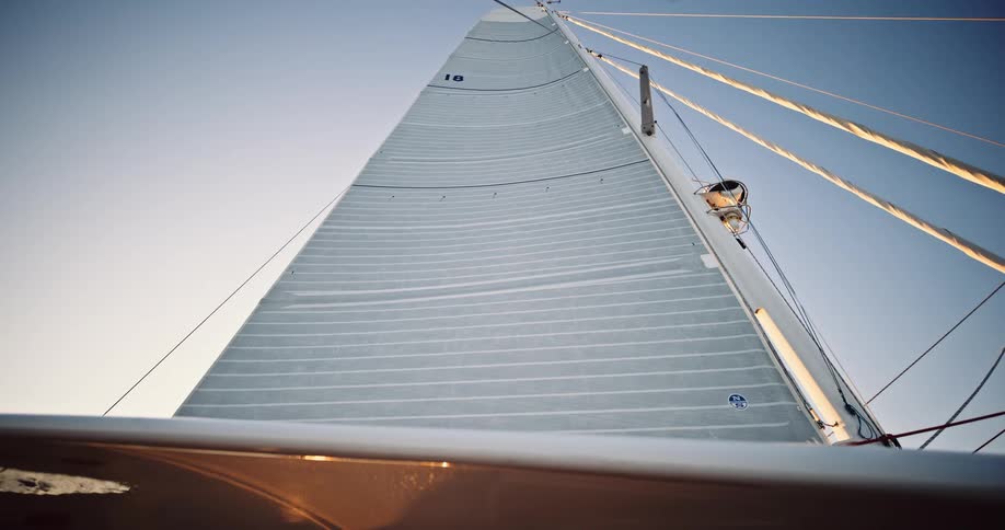 A serene cinemagraph captures a sailboat's mainsail full of wind, viewed from a low angle against a clear blue sky