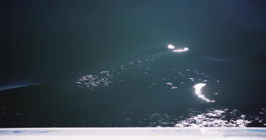 A mesmerizing high-angle shot of a boat wake creating shimmering, sunlit patterns on the surface of dark, calm water