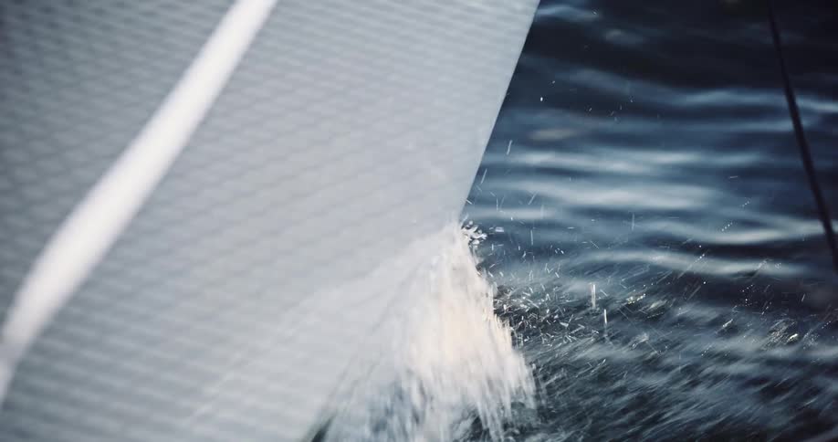 A slow motion close up of a sailboat's hull cutting through the water, creating a powerful splash