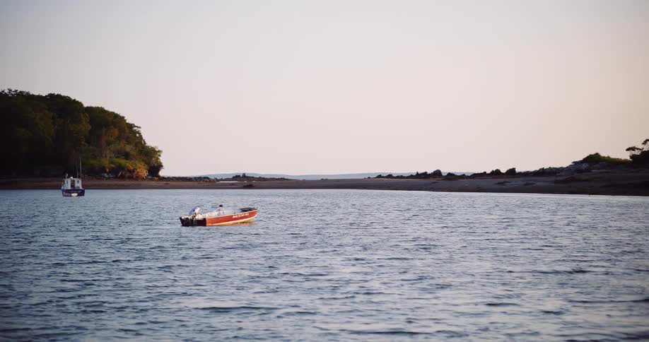 A tranquil scene of a small red motorboat anchored in a calm bay at dusk