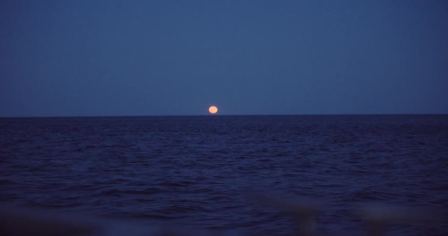 A serene view of the full moon rising over the deep blue ocean at night