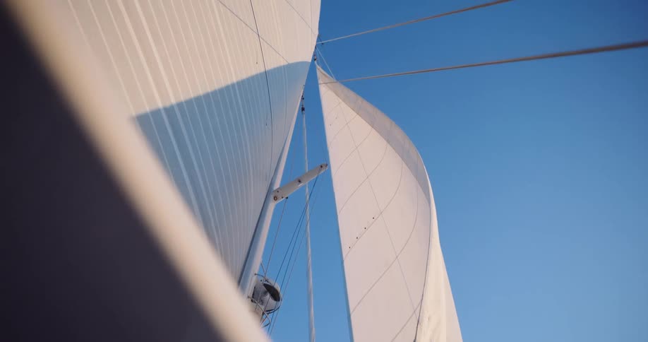 Looking up at the majestic white sails of a sailboat catching the wind against a perfect clear blue sky