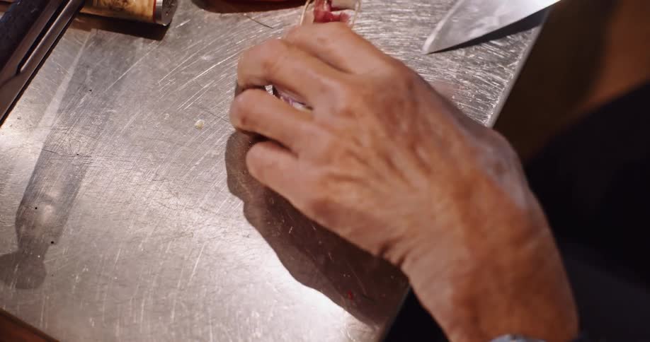 A close-up slow motion shot of a chef's hands slicing a purple shallot on a metal prep table