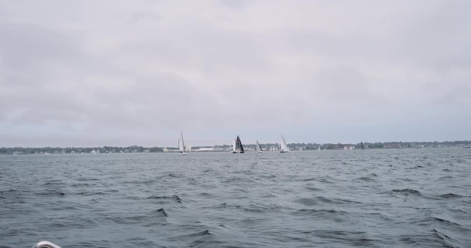 A fleet of sailboats races across a choppy bay under a blanket of thick, gray clouds