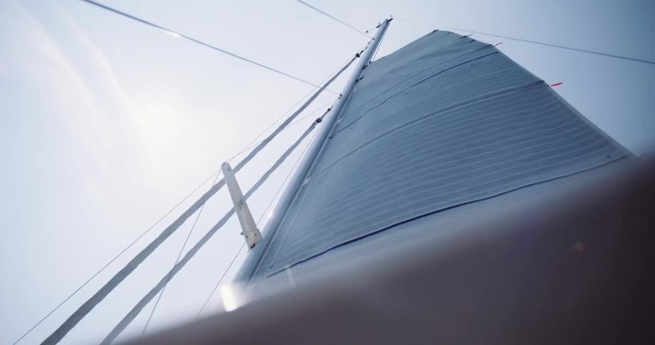 A low-angle view captures a sailboat's mast and full sail, number 18, gently blowing in the wind against a bright, clear sky