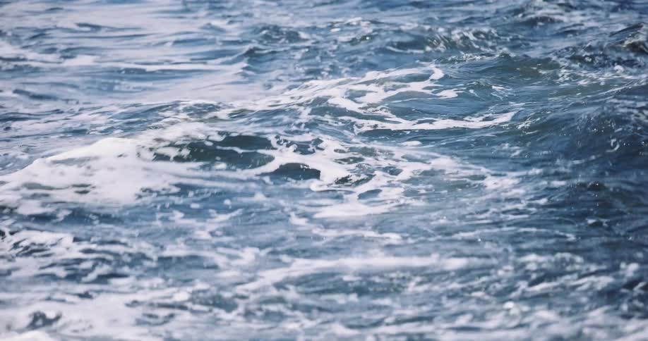 A slow-motion close-up of choppy blue ocean water churning with white foam