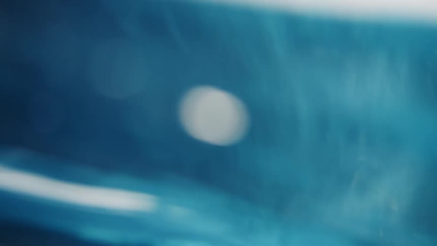 An ethereal underwater shot captures shimmering light rays and bubbles rising through clear blue water in slow motion
