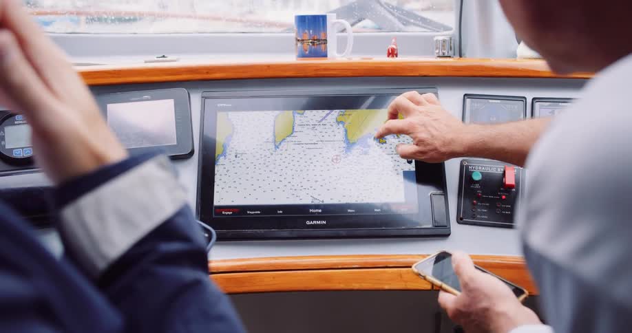 Two men use a touch-screen navigation system and smartphones to plot their course on a boat's bridge