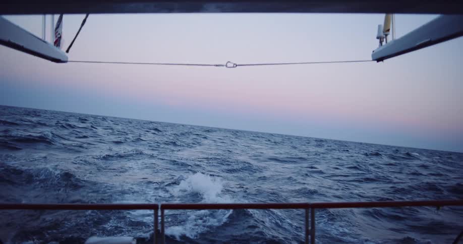 A slow-motion view from the back of a boat shows the wake churning in the open ocean against a beautiful pink and blue twilight sky