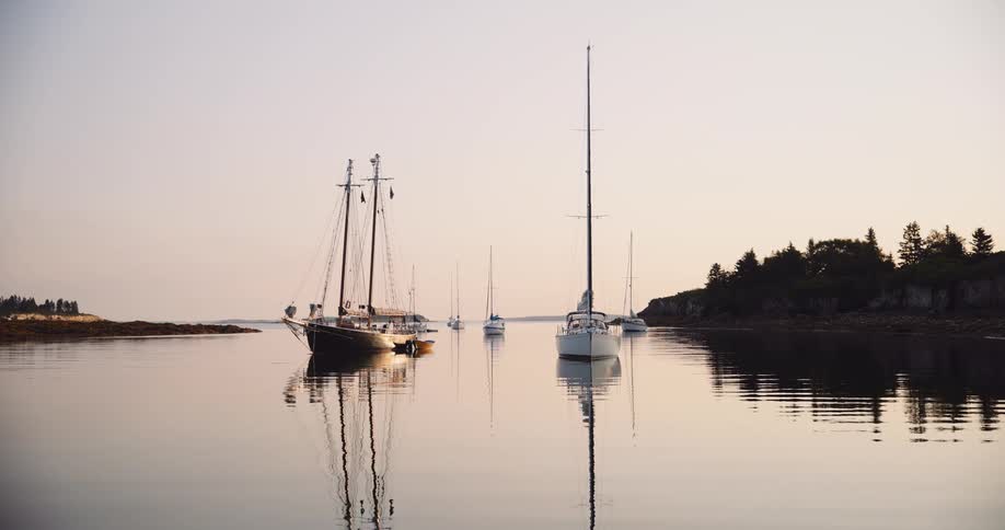 A tranquil scene of sailboats anchored in a still harbor at sunset, their reflections perfectly mirrored on the glassy water