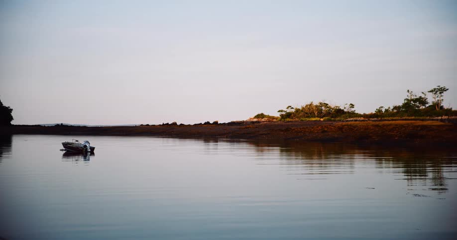 A lone motorboat floats on the calm, reflective waters of a bay at dusk