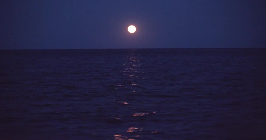 A bright full moon casts a glowing reflection across the dark, calm ocean at night