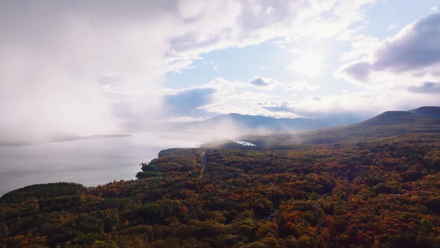 A majestic aerial view captures a misty lake and a vast autumn forest as sunlight breaks through the clouds