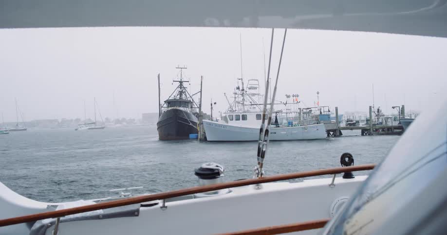 View from a sailboat deck of fishing trawlers docked in a harbor during a rainy day