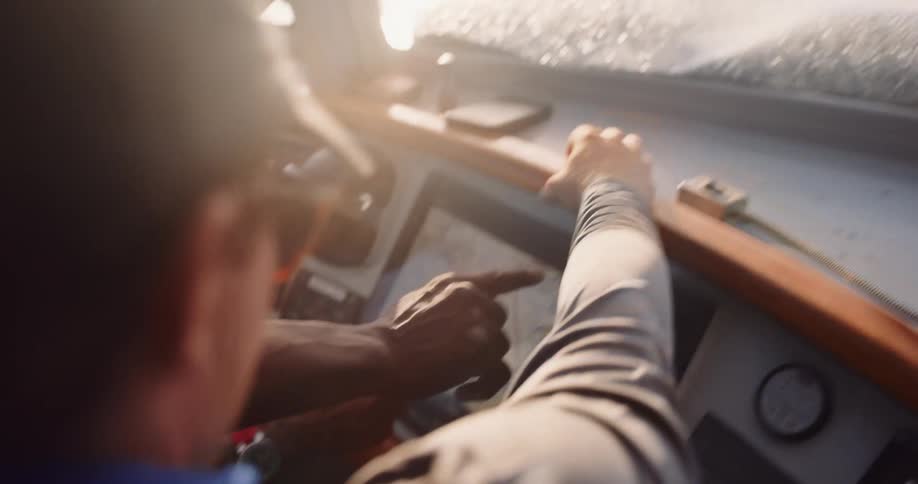 Two men collaborate at the helm of a moving boat, using a touchscreen GPS chart plotter to navigate their route in the bright sun