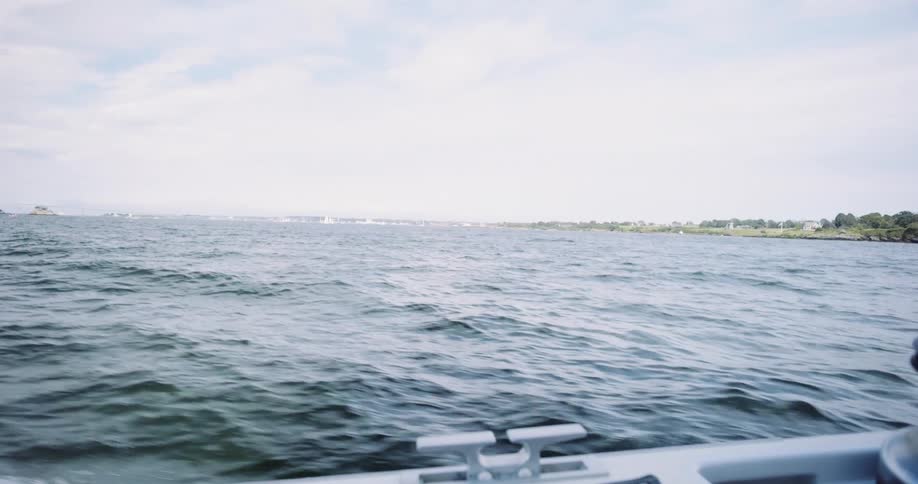 A serene point-of-view shot from a moving boat as it travels across the open water towards a distant shoreline on a bright day