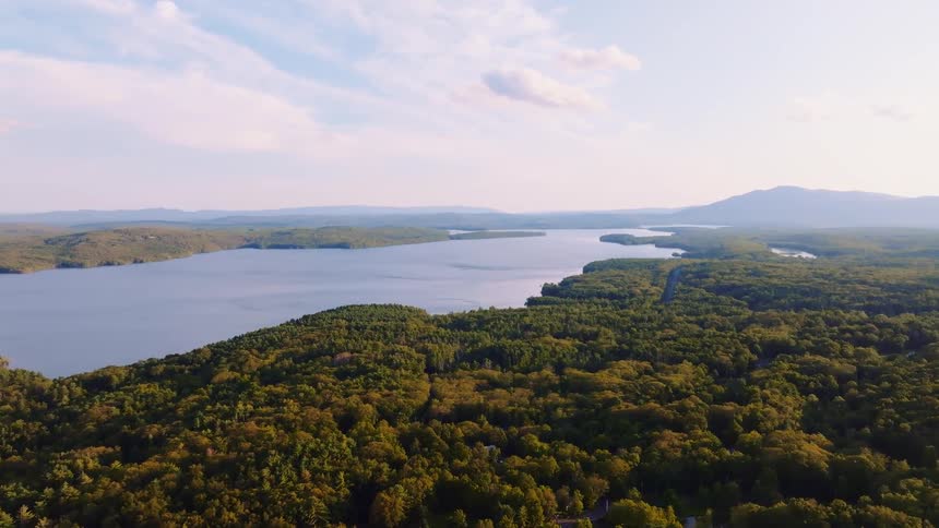 A beautiful aerial shot of a serene lake bordered by a vast green forest with mountains in the distance