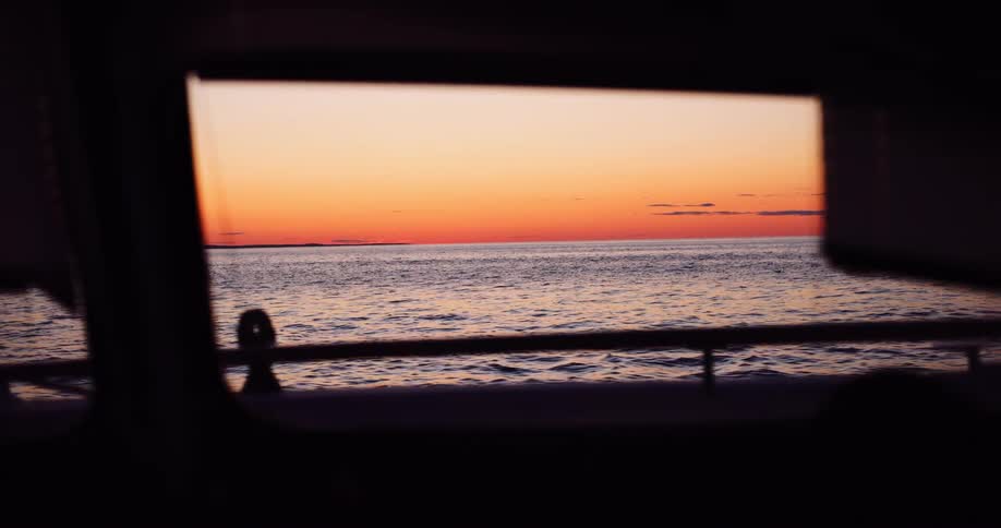 A serene view of the calm ocean at sunset, seen through the window of a moving boat