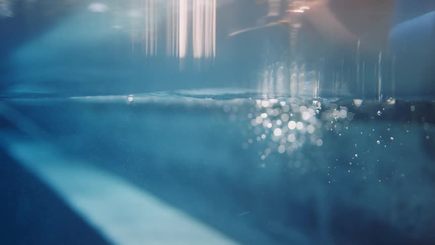 A tender split-level, slow-motion shot shows a father sitting by the pool holding his child's hand as they learn to swim