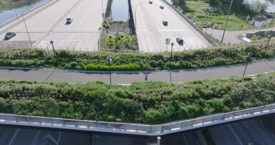 High-angle aerial view of a person running on a green pedestrian overpass above a busy multi-lane highway on a sunny day