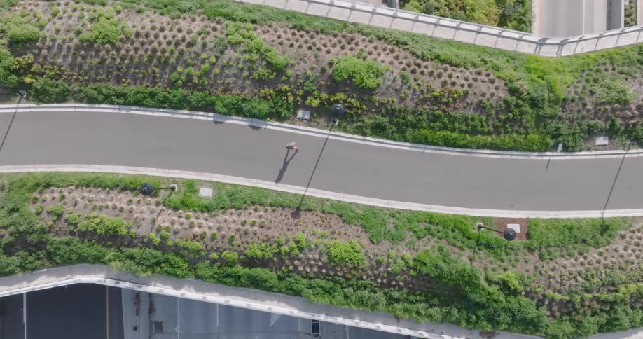 A top-down aerial view of a person running on a modern green bridge over a busy highway, highlighting sustainable urban architecture