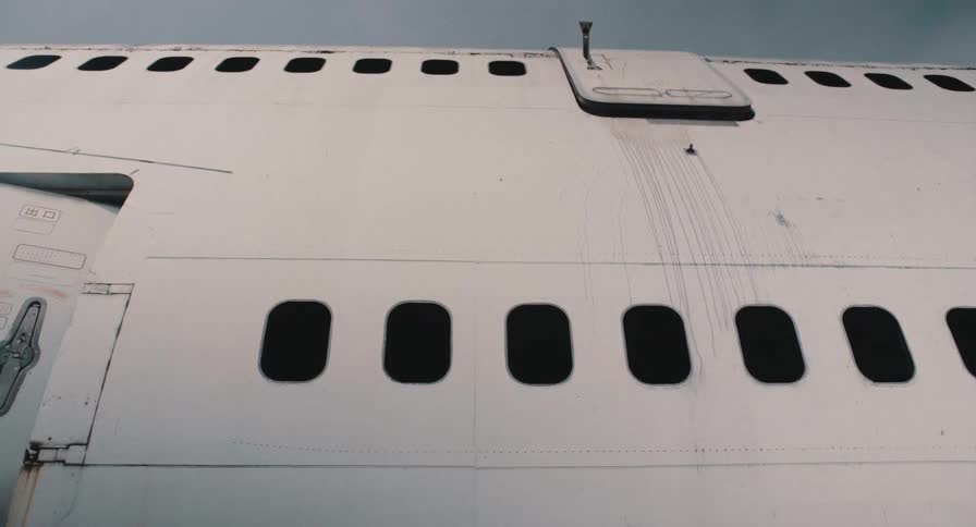 A static low-angle view of the weathered white fuselage of an old, abandoned airplane