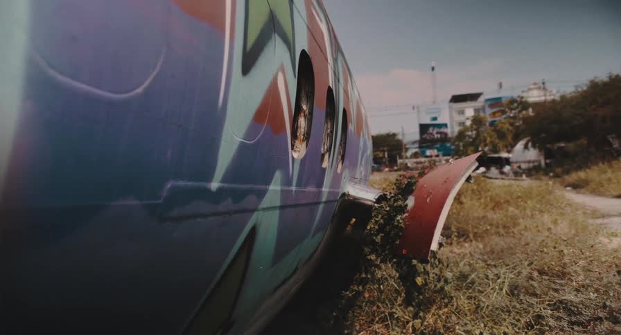 Low-angle static shot of a wrecked and graffiti-covered airplane lying abandoned in an overgrown field