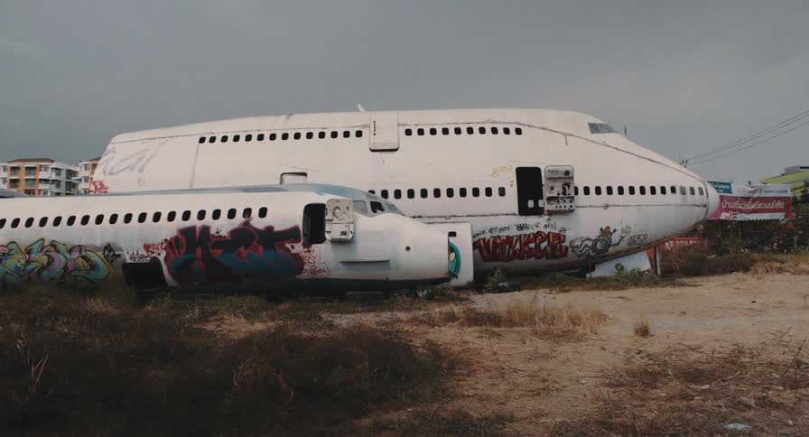 Two abandoned and graffiti-covered airplane fuselages rest in a desolate junkyard under a grey sky