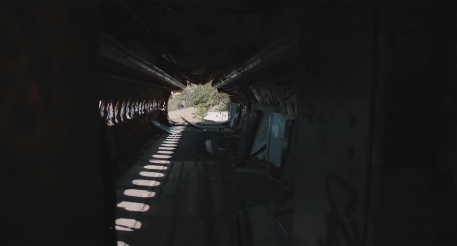 A static shot from inside the dark, derelict fuselage of an abandoned airplane looking towards the light