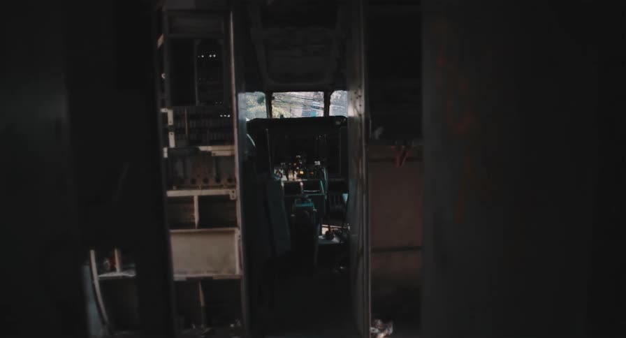 A slow, unsettling pull-back shot from within a dark, derelict vehicle reveals the decaying control room