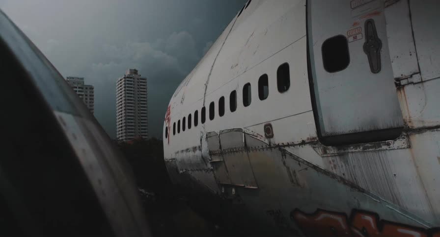 A dystopian time-lapse of a decaying airplane fuselage with a stormy sky and city skyline in the background