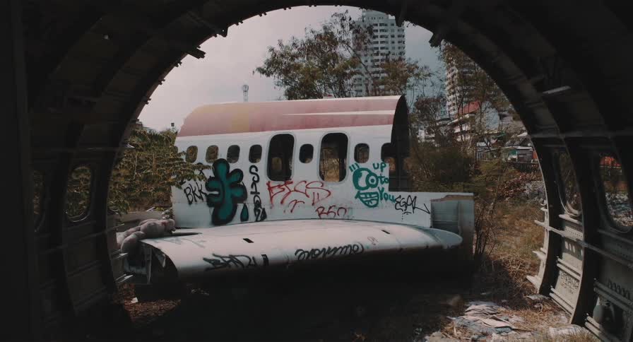 A view from inside the fuselage of an abandoned airplane looking out at another wrecked fuselage covered in graffiti in an airplane graveyard