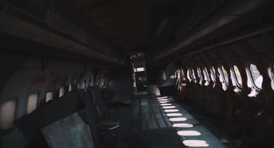 Sunlight filters into the dark, desolate interior of a derelict airplane fuselage
