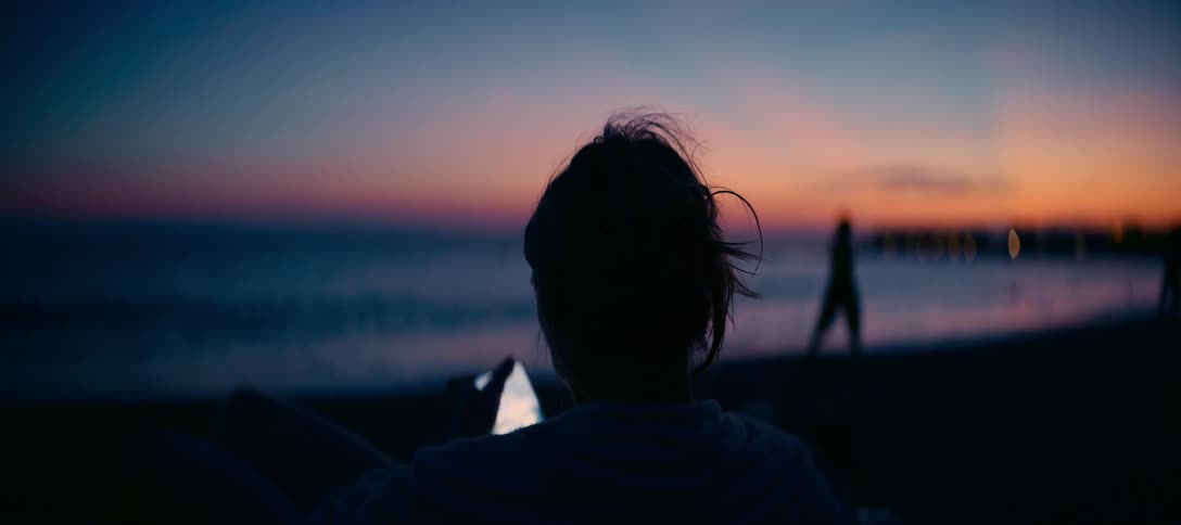 Rear view of a silhouetted woman relaxing on the beach and using her phone during a beautiful sunset