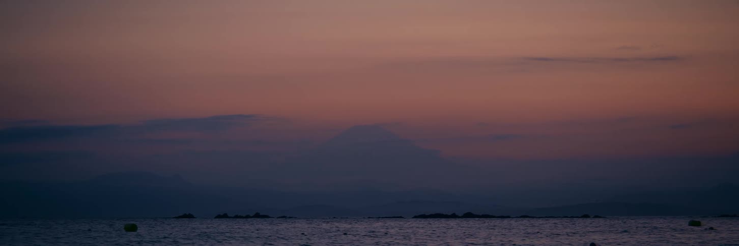 The majestic silhouette of Mount Fuji stands against a beautiful pink and purple sunset sky over the calm sea