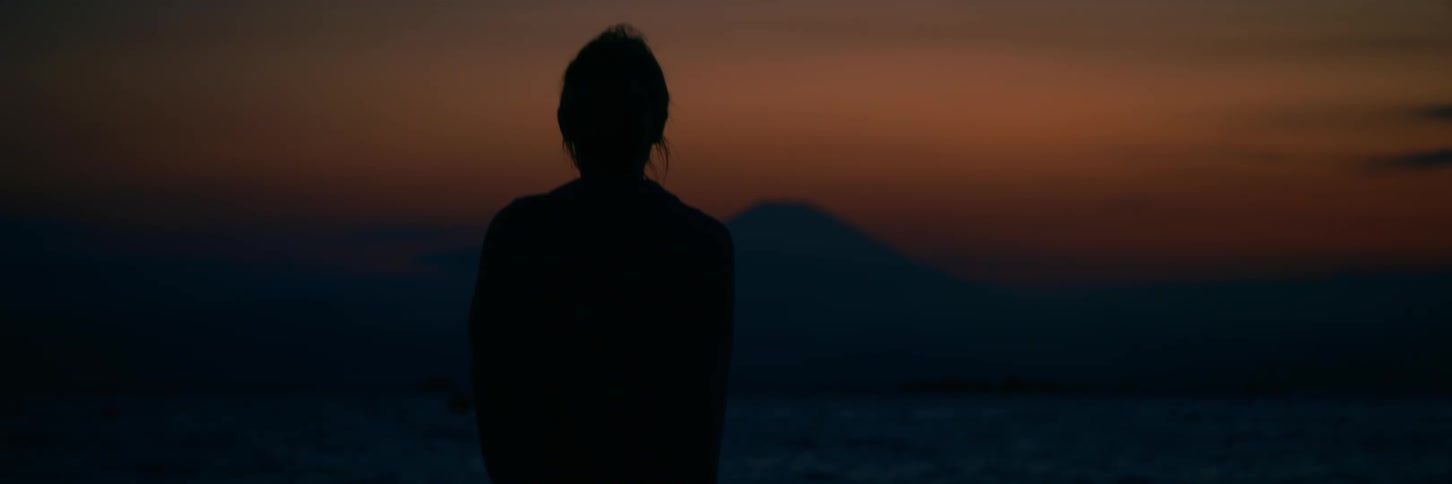 A silhouetted person stands peacefully, watching a beautiful sunset over the ocean with Mount Fuji in the distance