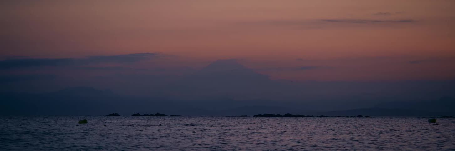 The majestic silhouette of Mount Fuji stands against a colorful dusk sky over the tranquil ocean