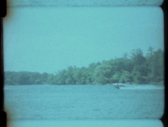 Vintage 8mm footage captures a speedboat cruising across a wide, tree-lined river on a summer day