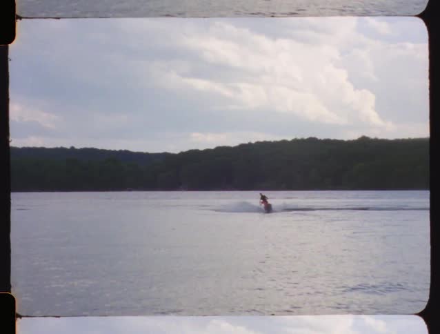 Vintage 8mm film captures a person riding a jet ski across a lake and then falling into the water