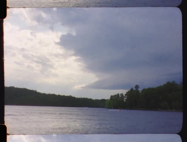 A jet ski makes its way across a calm lake under a cloudy, stormy sky in this vintage footage