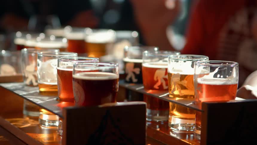 A close-up shot of beer tasting flights with various craft beers sitting on a sunny bar top in a brewery