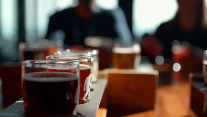Close-up of a craft beer tasting flight on a sunlit table with friends enjoying a conversation in the background