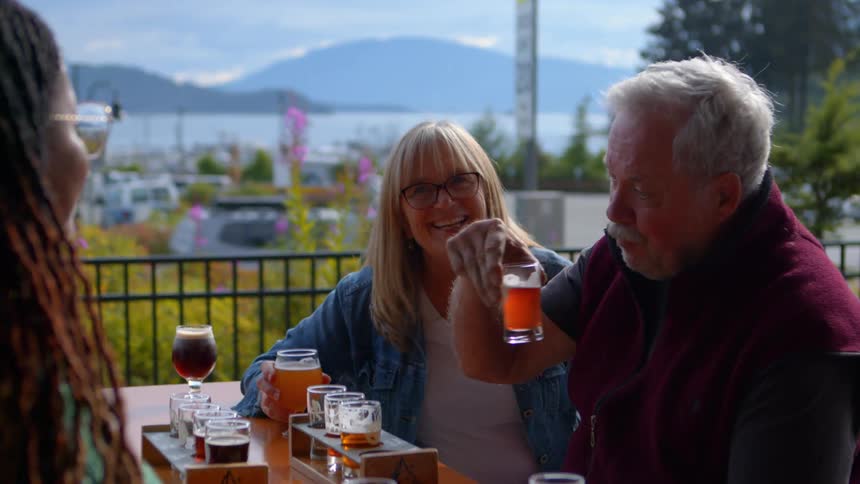 A diverse group of friends enjoy a flight of craft beer on an outdoor brewery patio overlooking a scenic marina