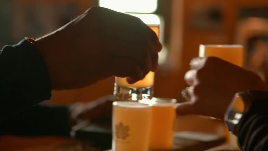 A group of friends toast their glasses of craft beer from a tasting flight in a dimly lit brewery