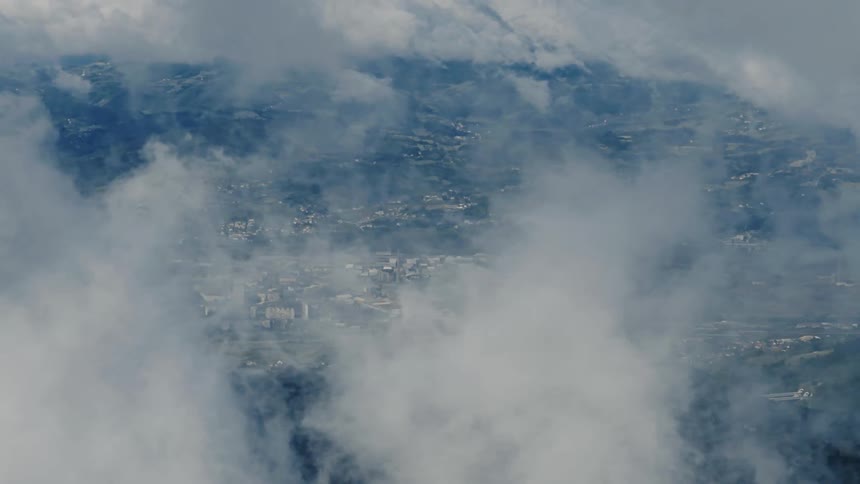 Dreamy aerial view of a city in a valley peeking through a thick layer of moving clouds