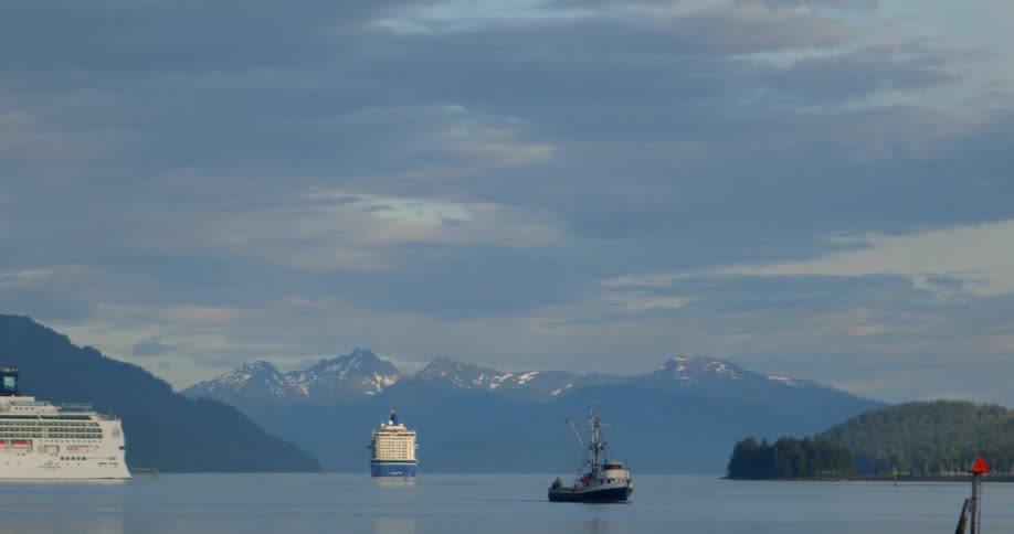 A serene view of cruise ships and a fishing boat floating on calm waters with a majestic snow-capped mountain range in the background