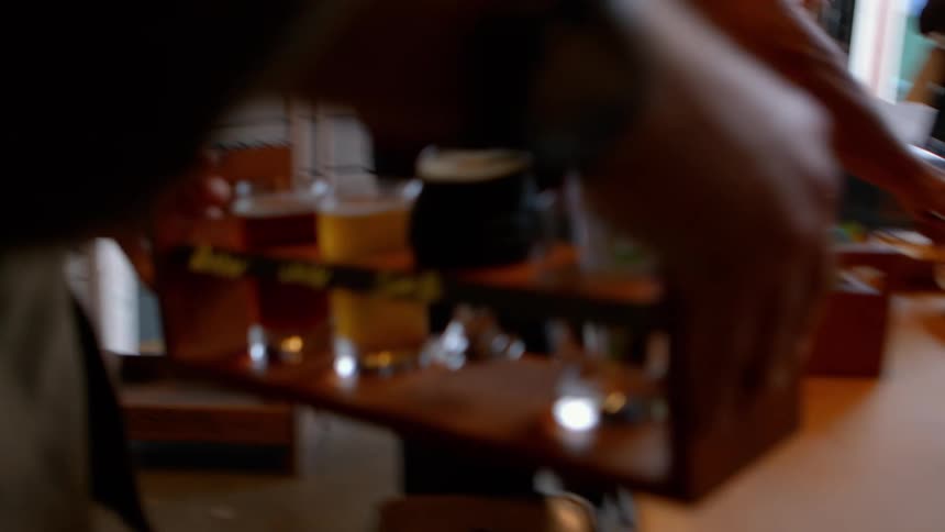 A man walks through a brewery with a flight of craft beer and sets it on a table for a tasting