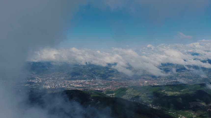 A majestic aerial perspective looking down through the clouds at a city and industrial area in a vast green landscape