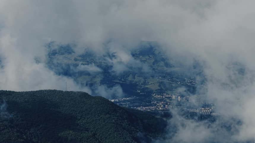 A stunning high-angle view shows a city in a valley partially obscured by thick, slow-moving clouds